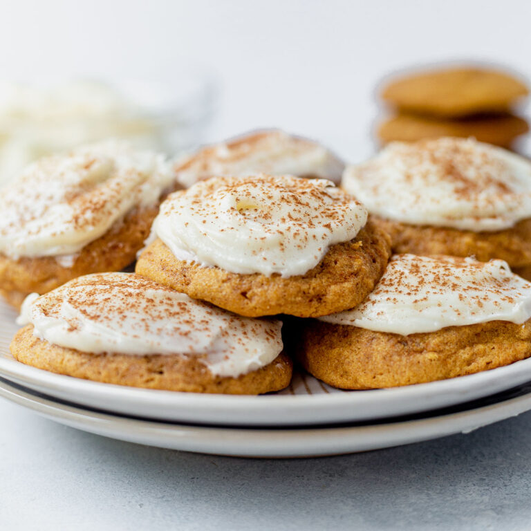 a stack of pumpkin cookies with cream cheese frosting on a white plate