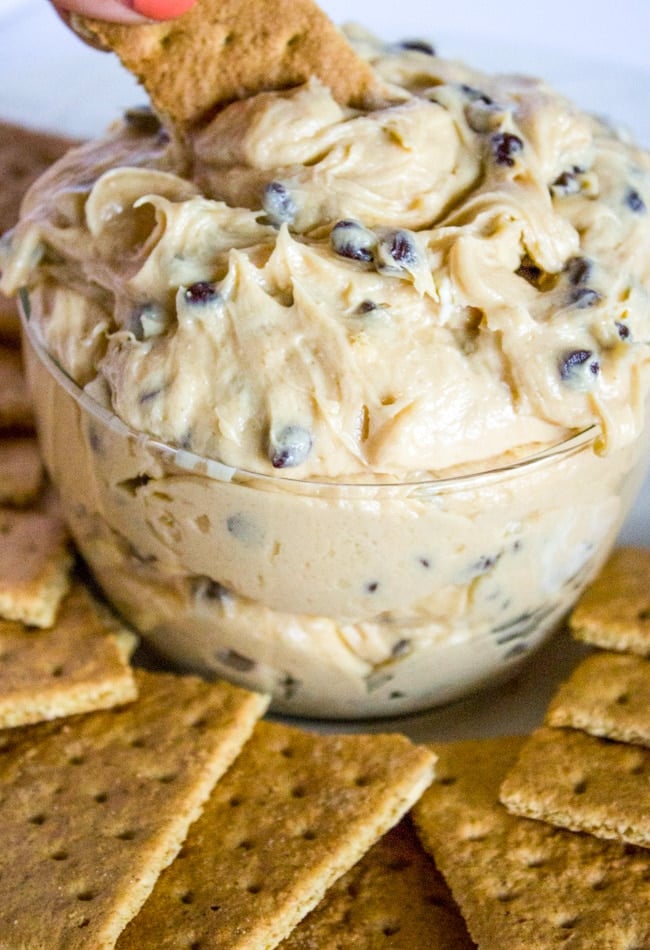 a hand with a graham cracker dipping into buckeye dip and chocolate chips in a bowl with graham crackers fanned around the bottom