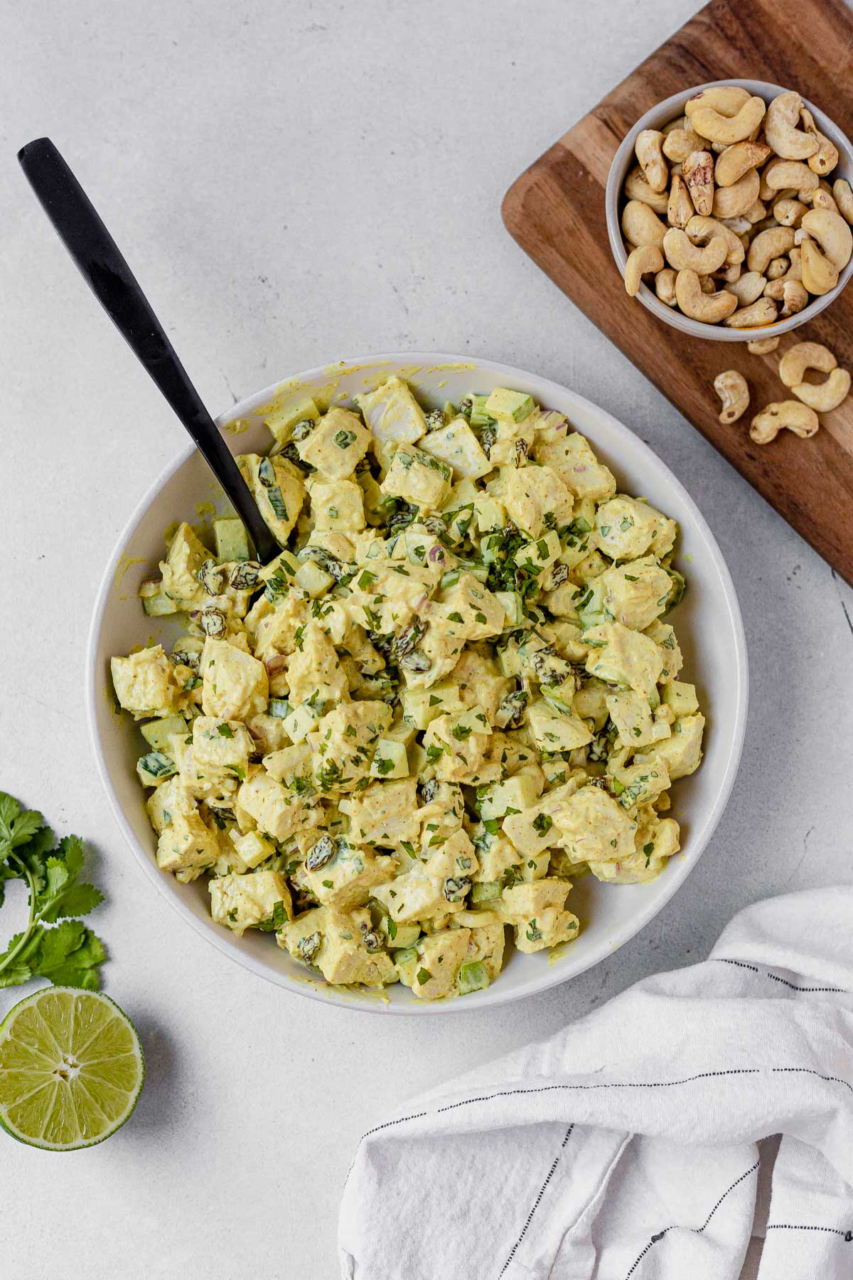 curry chicken salad topped with cilantro in a white bowl with a serving spoon