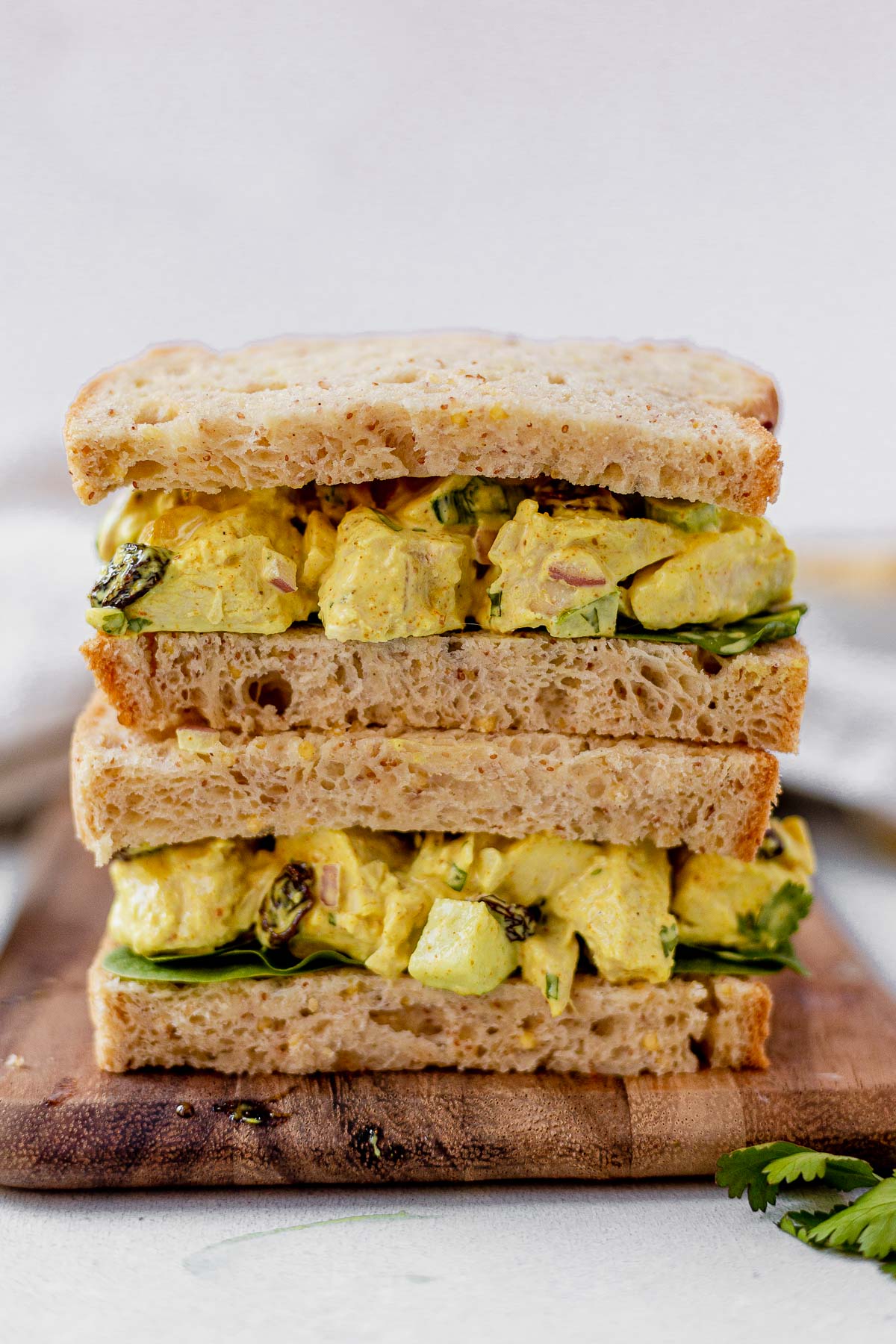 curry chicken salad sandwich sliced in half and stacked on a wood plate