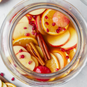 apple cider sangria in a glass pitcher full of apple slices and cinnamon sticks