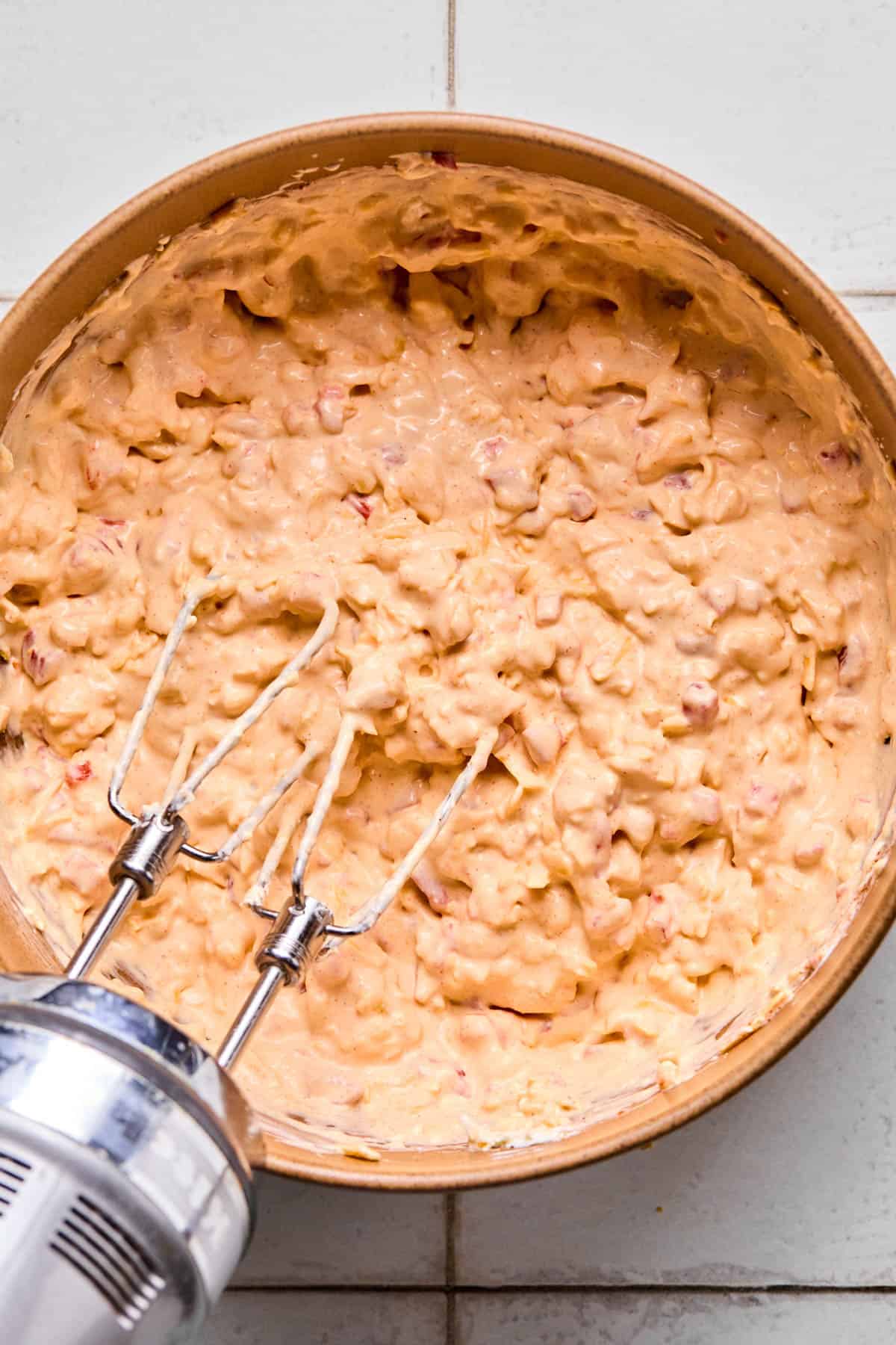 ingredients for pimento cheese dip all mixed together with the beaters of a hand mixer still in the bowl.