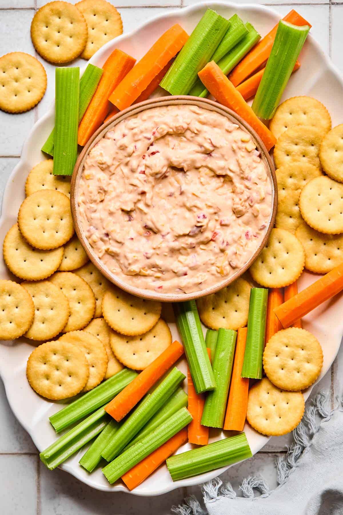 pimento cheese dip in a bowl surrounded by Ritz crackers and carrot and celery sticks