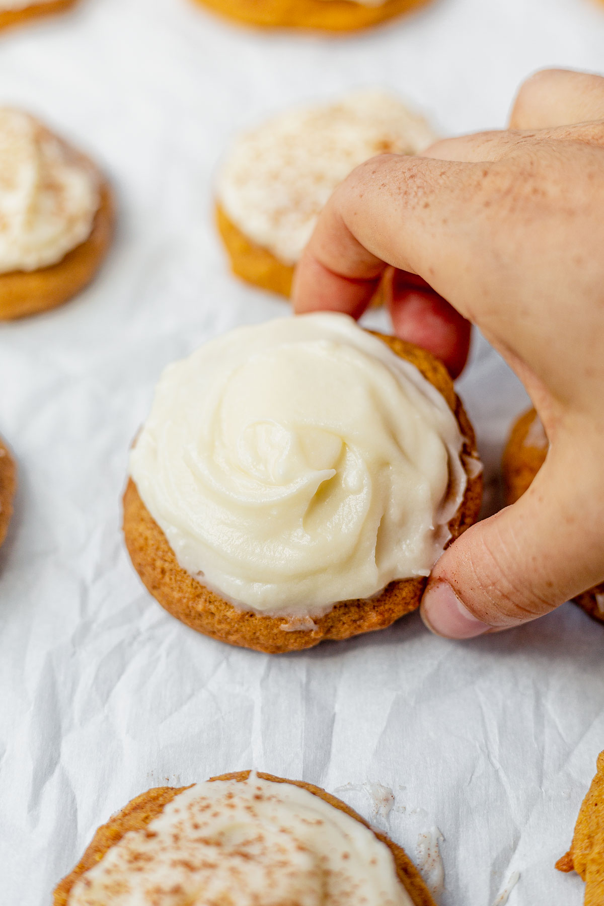hand picking up a soft pumpkin cookie with cream cheese frosting