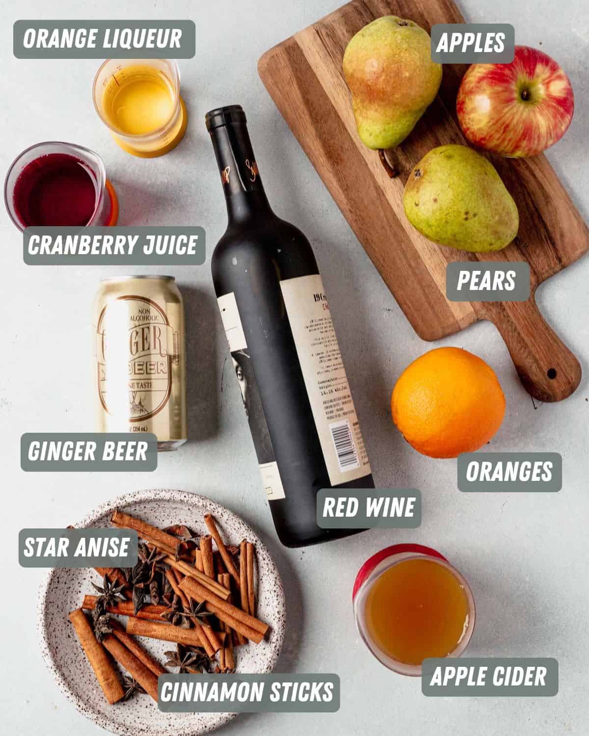 a bottle of red wine, orange, apples, apple cider, cranberry juice and cinnamon sticks on a table