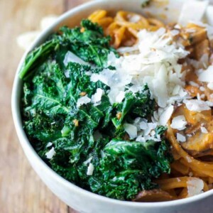 kale mushroom pasta with fresh grated parmesan in a bowl on a wooden counter