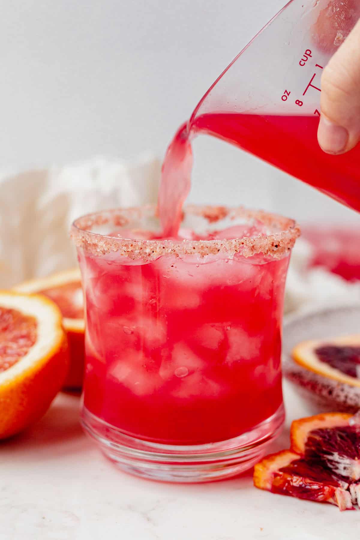 pouring a blood orange margarita into a glass with ice