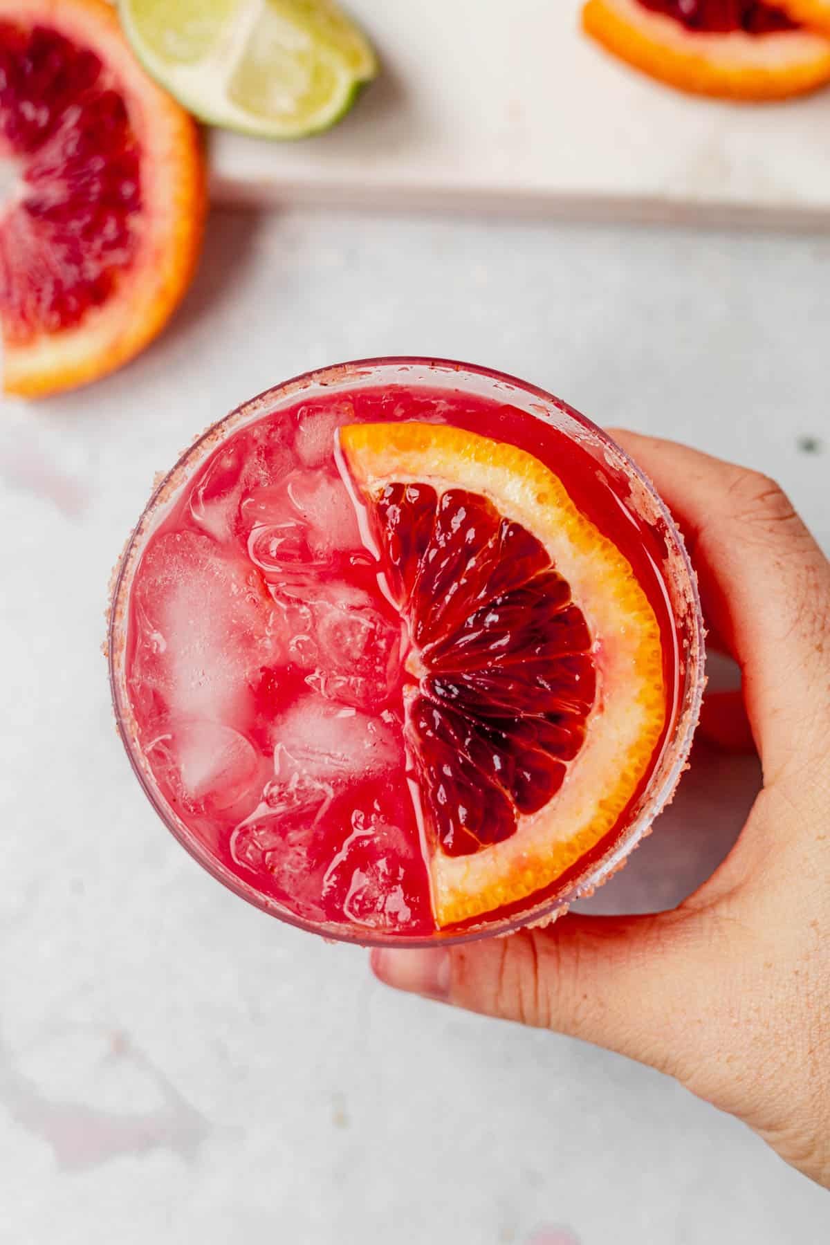 a hand holding a blood orange margarita