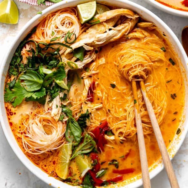 thai curry noodle soup in a bowl with fresh herbs and chopsticks