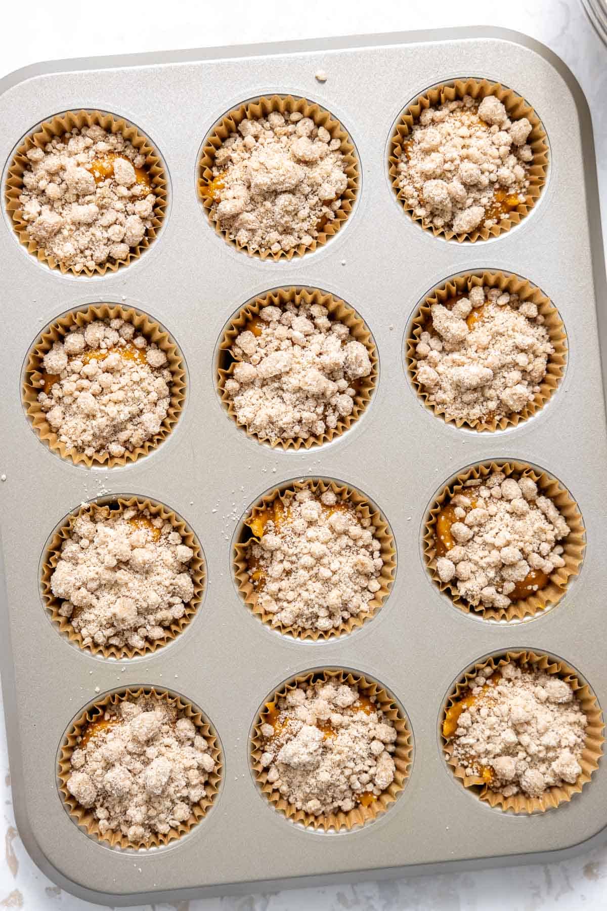 pumpkin muffin batter topped with streusel in muffin cups. 