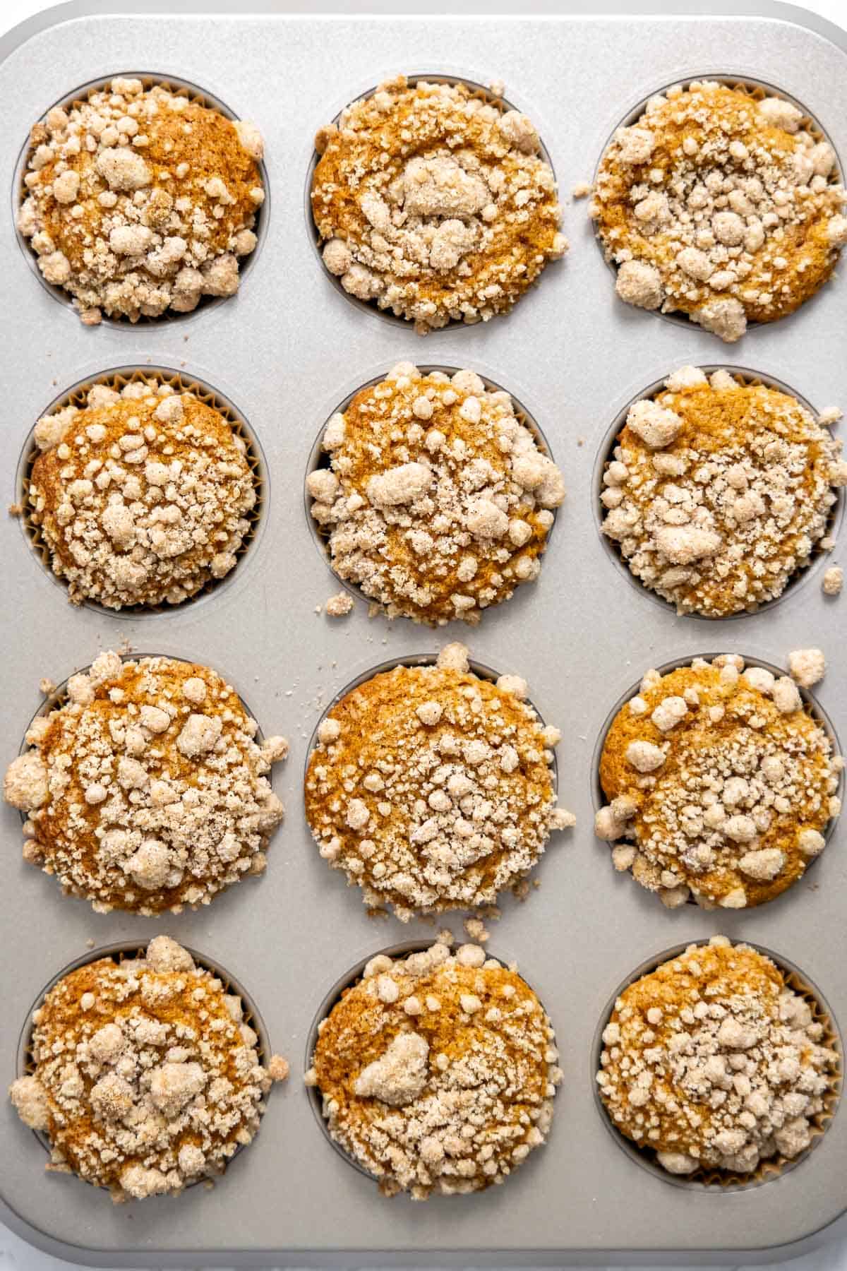 baked pumpkin streusel muffins cooling in a muffin tin.