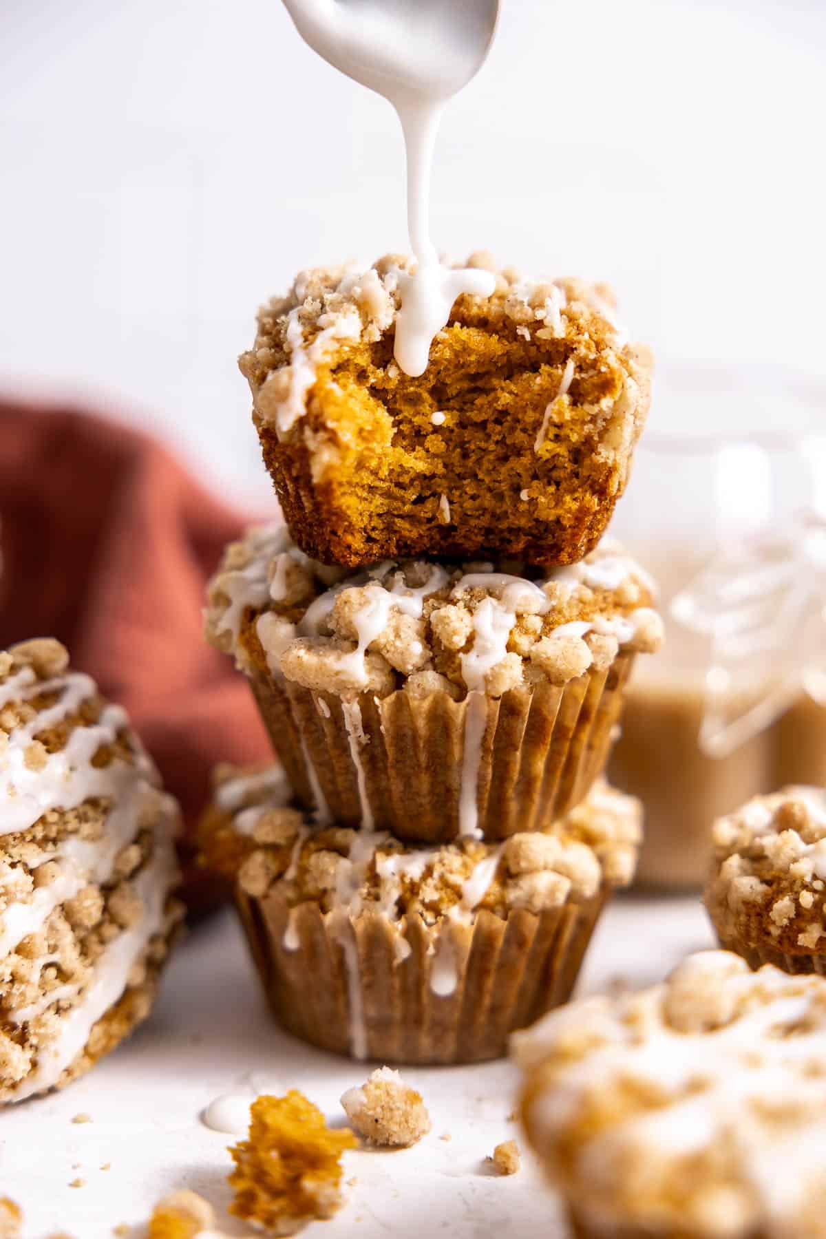 a stack of three pumpkin streusel muffins with icing.