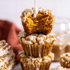 a stack of three pumpkin streusel muffins with icing drizzled on top.