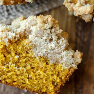 pumpkin muffin cut in half on the table so you can see the pumpkin muffin and streusel layers