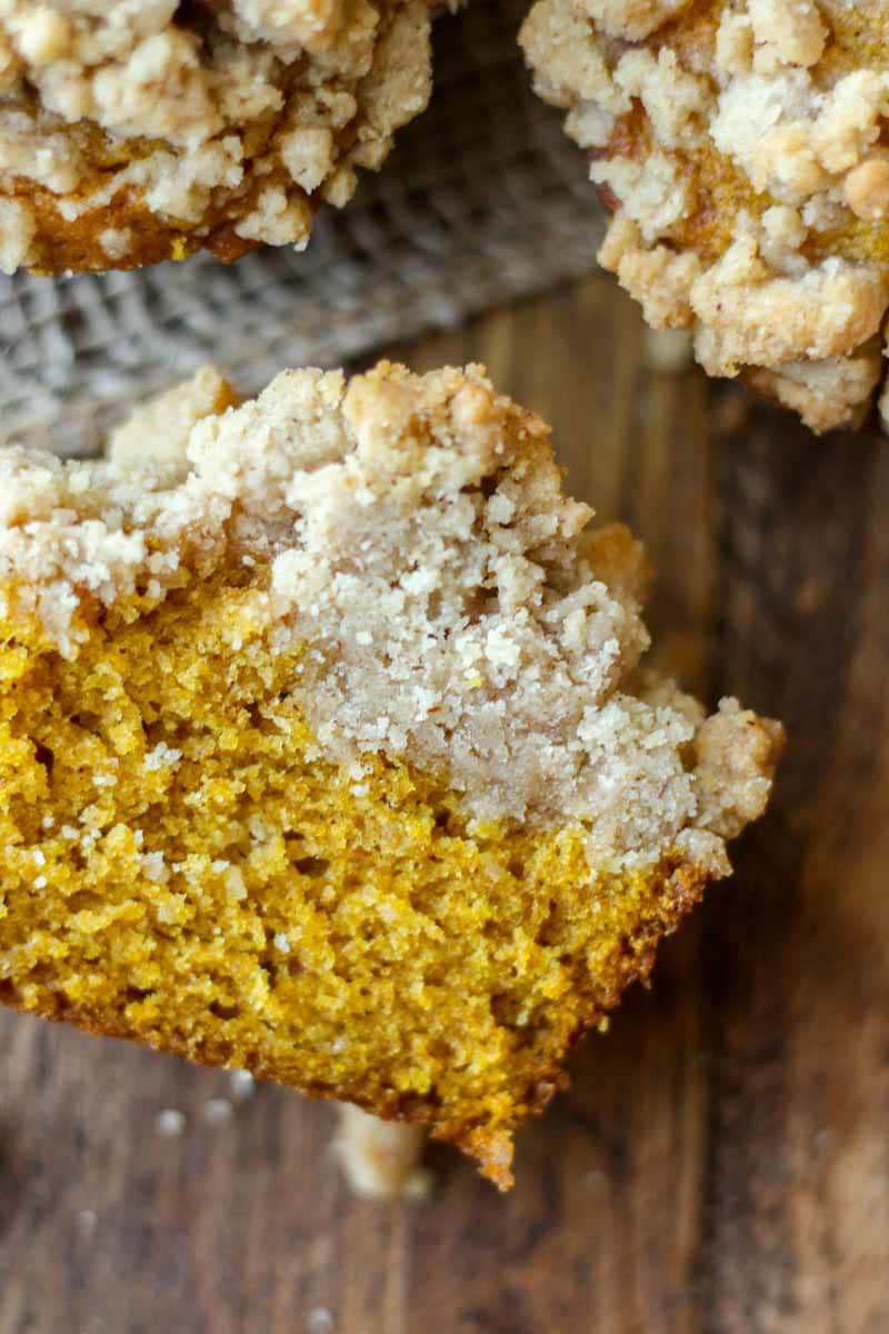 pumpkin muffin cut in half on the table so you can see the pumpkin muffin and streusel layers