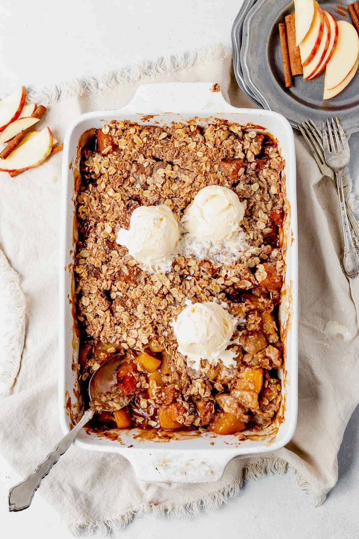 peach and apple crisp in a white 9x14 inch baking dish with 3 scoops of vanilla ice cream
