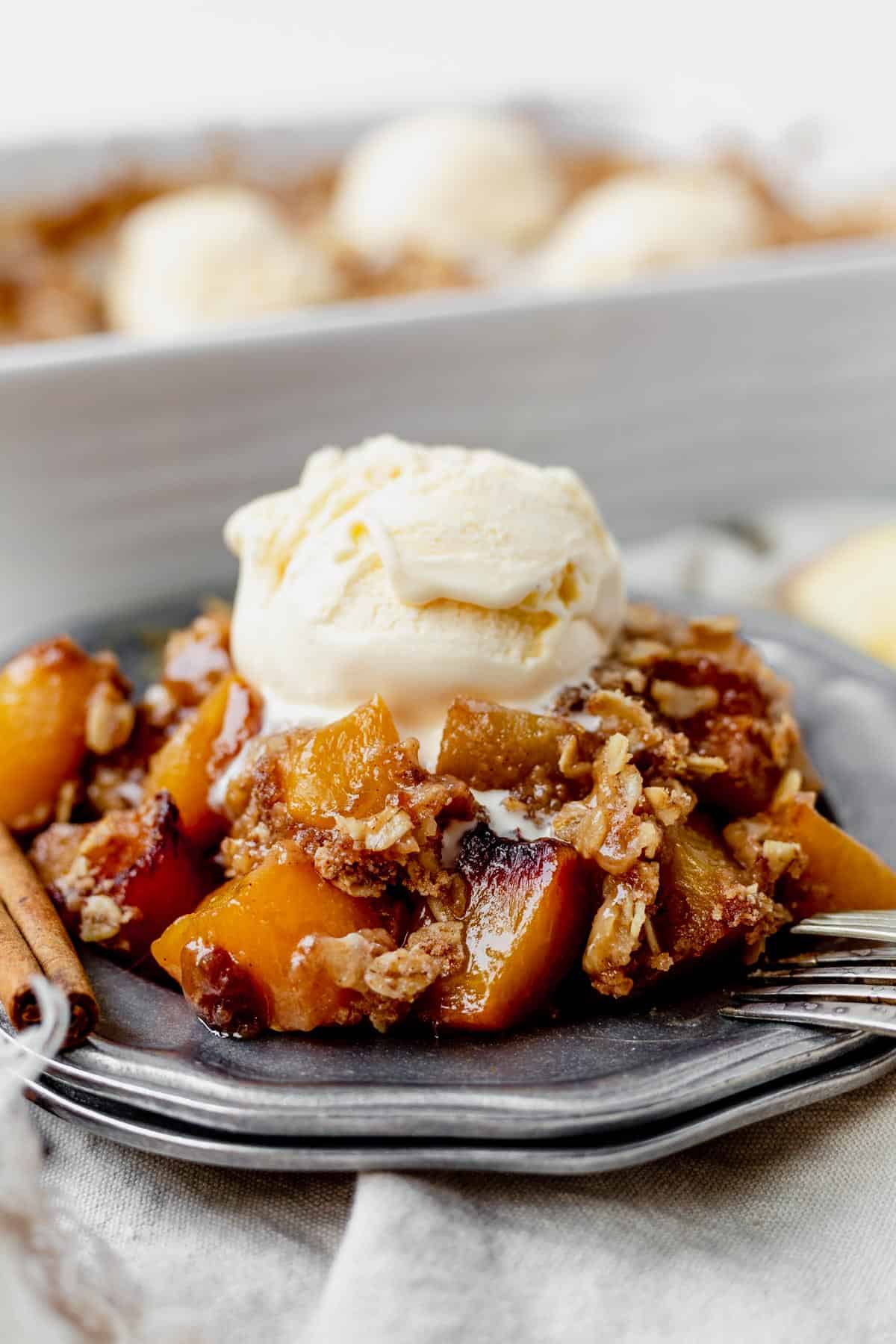 peach apple crisp on a metal plate with a scoop of ice cream