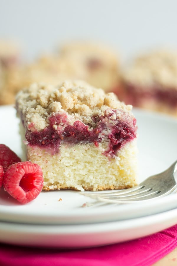 raspberry coffee cake on a white plate with fresh raspberries and a fork