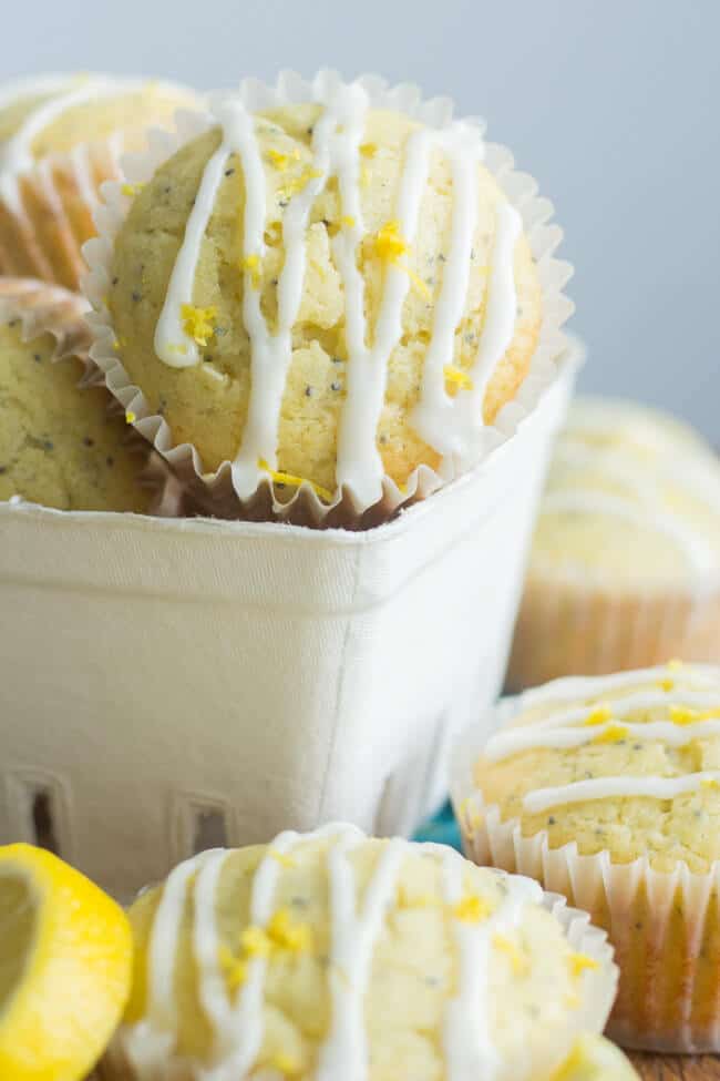 Healthier lemon poppy seed muffins stacked in a carton on a counter with more muffins surrounding it