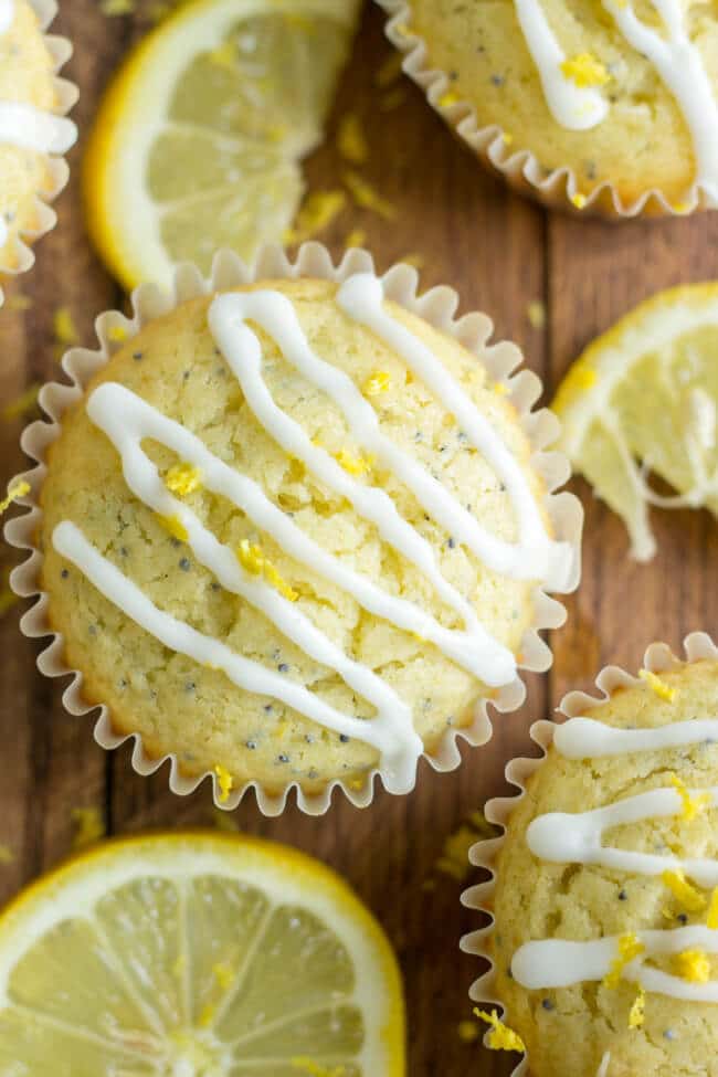 Glazed healthier lemon poppy seed muffins on a cutting board with lemon slices