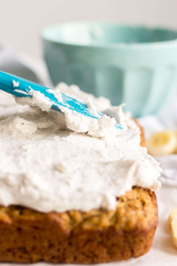 spatula spreading coconut whipped cream over healthy banana cake