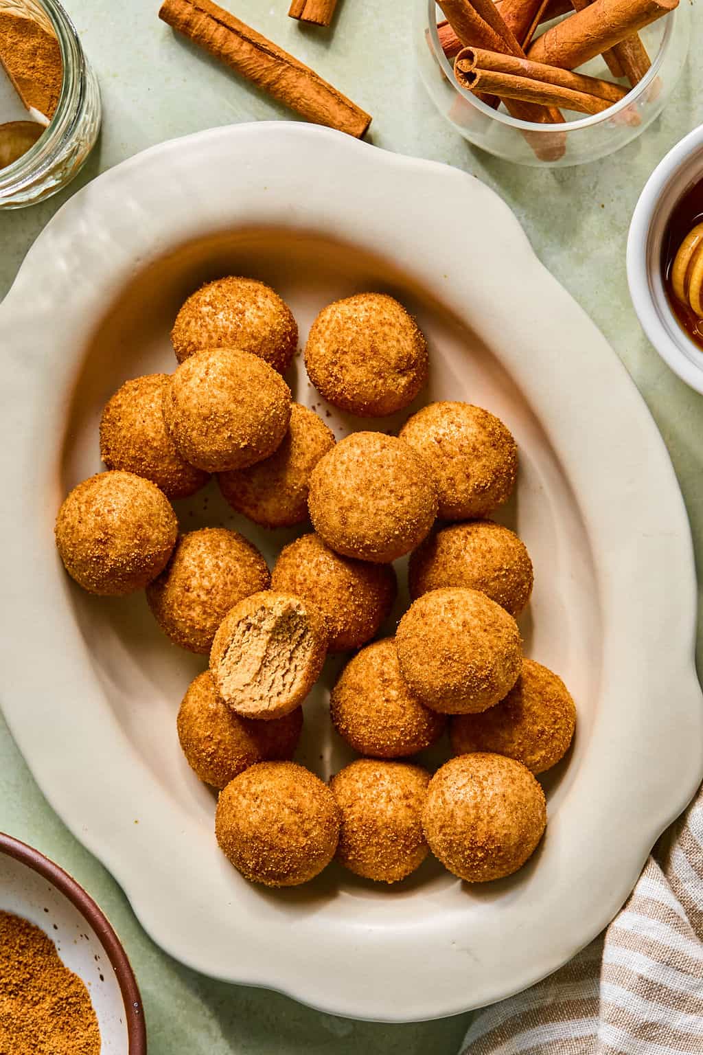A plate of round snickerdoodle protein balls, some with a cinnamon sugar coating and a few snickerdoodle protein balls around the plate.