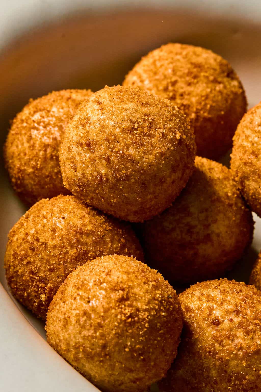 A close-up of several cinnamon sugar coated, round snickerdoodle protein balls stacked in a white bowl.