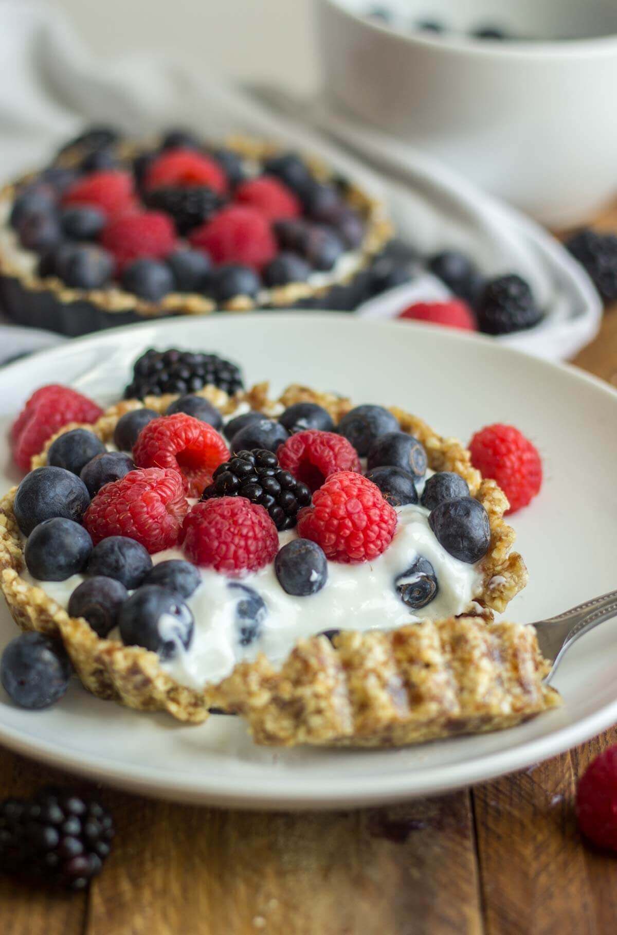 Fork digging into mini greek yogurt fruit tart filled with fresh berries