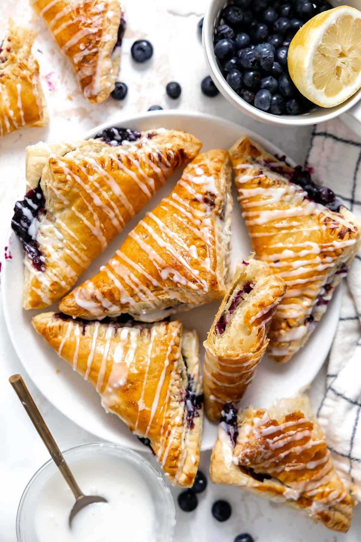 a serving plate of blueberry puff pastry turnovers with glaze.