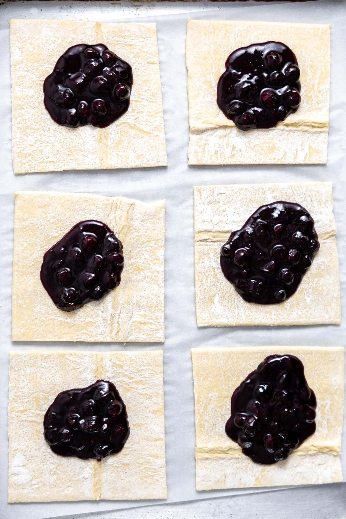 blueberry filling inside squares of puff pastry on  a baking sheet.