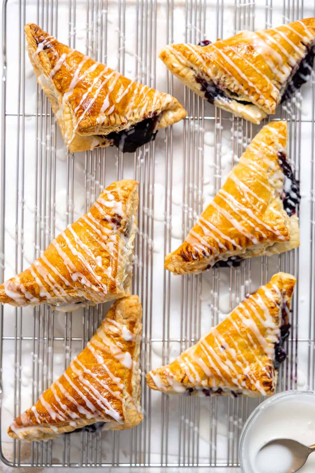 blueberry turnovers on a cooling rack with glaze drizzled on top.