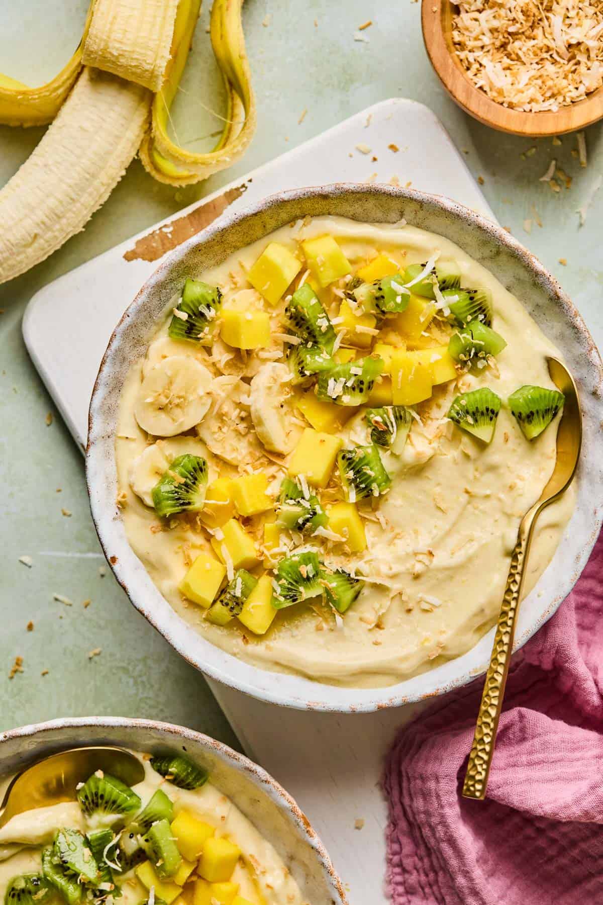 coconut smoothie bowl with toppings on a counter next to a peeled banana and bowl of toasted coconut 