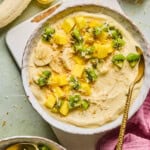 tropical smoothie bowl with pineapple, kiwi, and banana on top wtih a spoon dug into the bowl