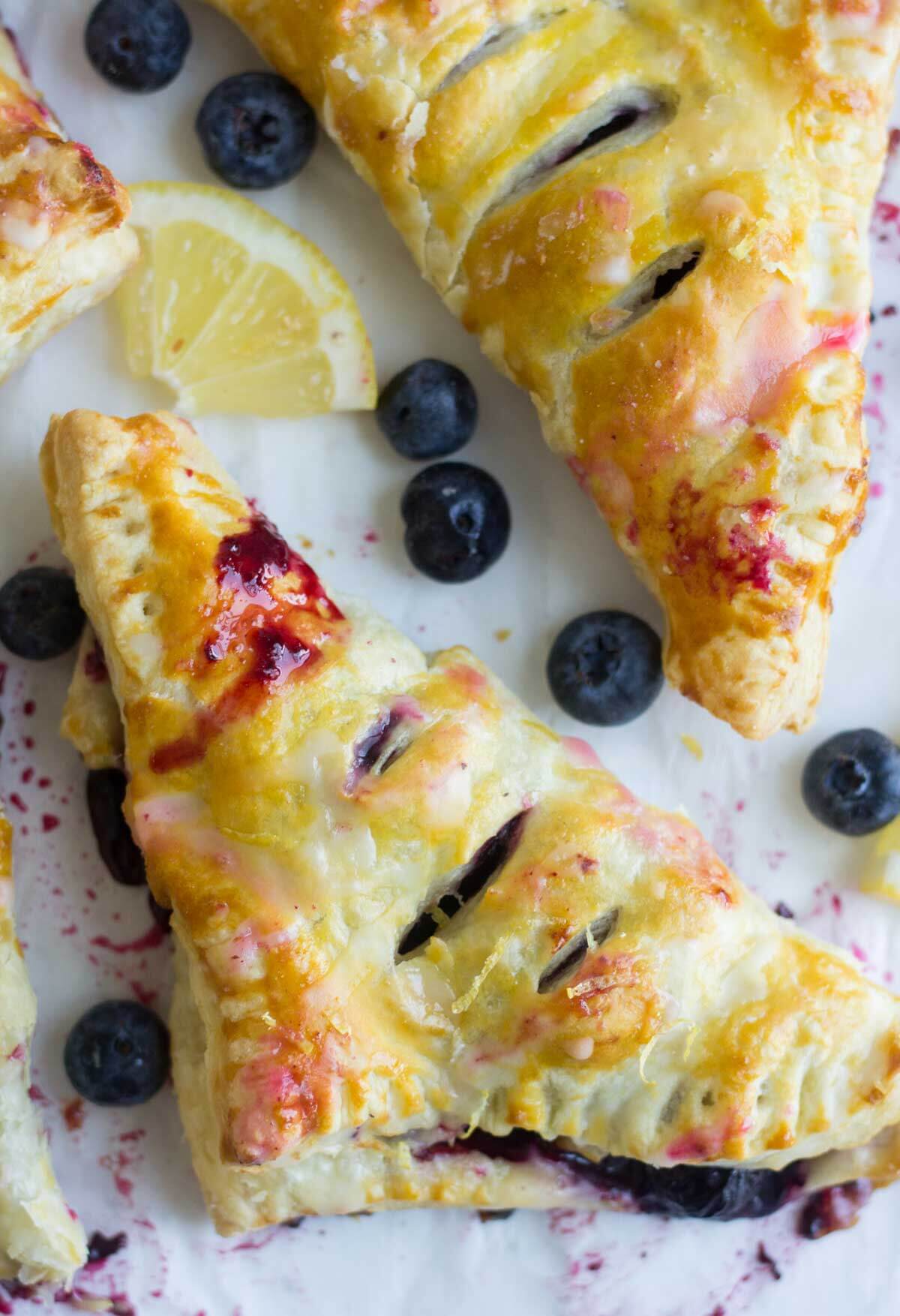 a blueberry turnover laying on parmchment paper surrounded by fresh blueberries