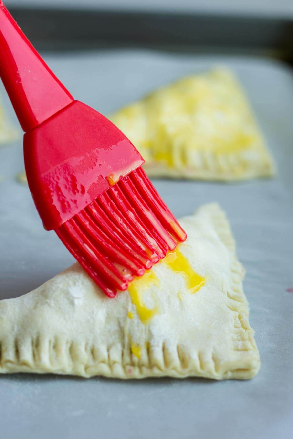 brushing egg wash over blueberry turnovers before going in the oven