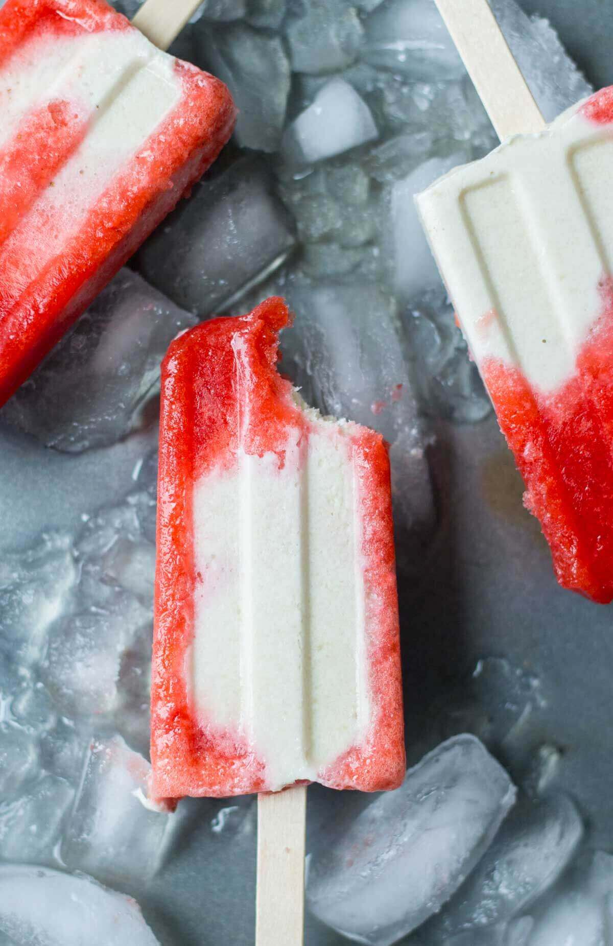 a bite taken out of a Strawberries and Cream Vegan Popsicle laying on ice