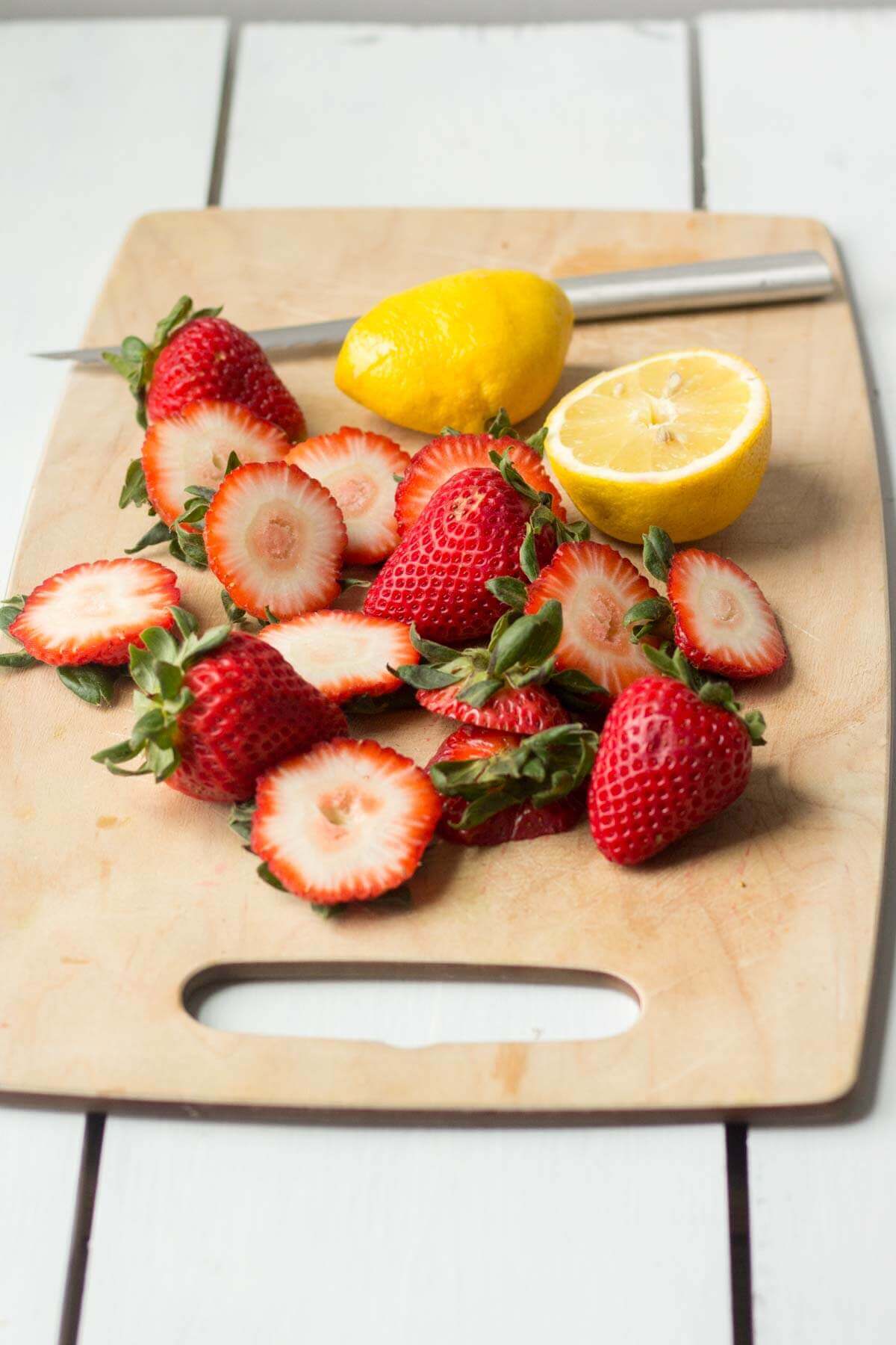 strawberries and lemon cut up next to a knife on a cutting board