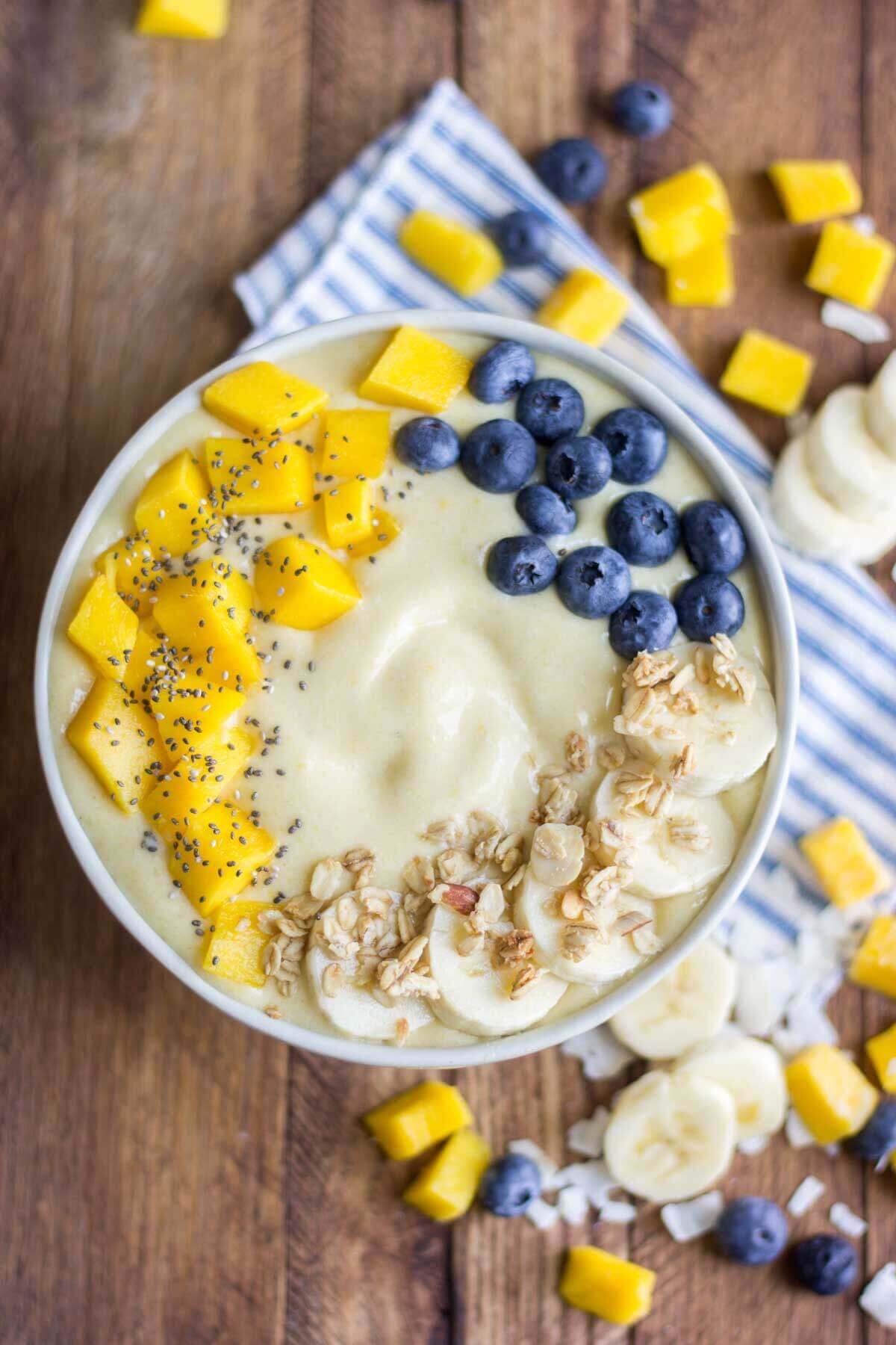 coconu smoothie bowl in a white bowl topped with mango, banana, blueberry and chia seeds