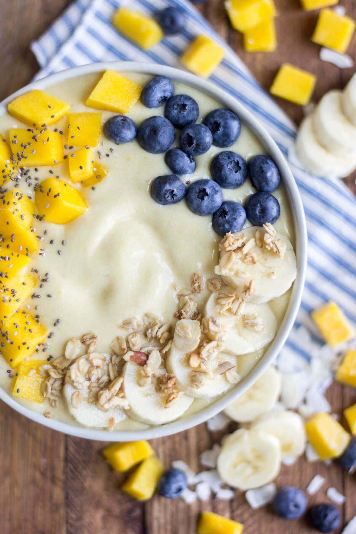 thick and creamy coconut smoothie in a bowl with mango, chia seeds, banana and blueberries on top