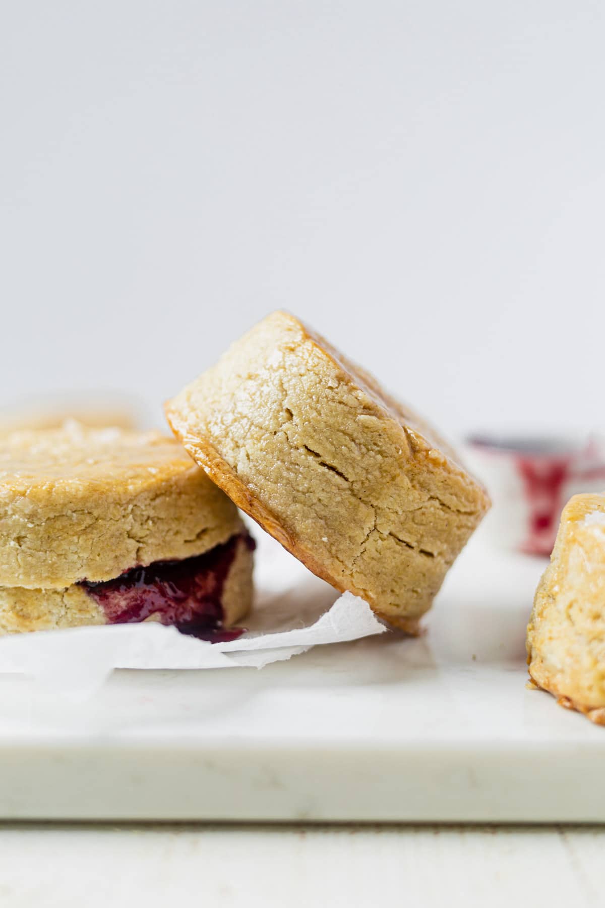 a flaky vegan biscuit with layers that's leaning up against another biscuit that's filled with fresh jam