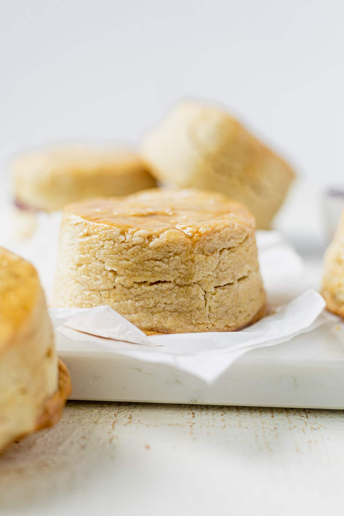 a thick and flaky vegan buttermilk biscuit on a piece of parchment paper with more biscuits around it