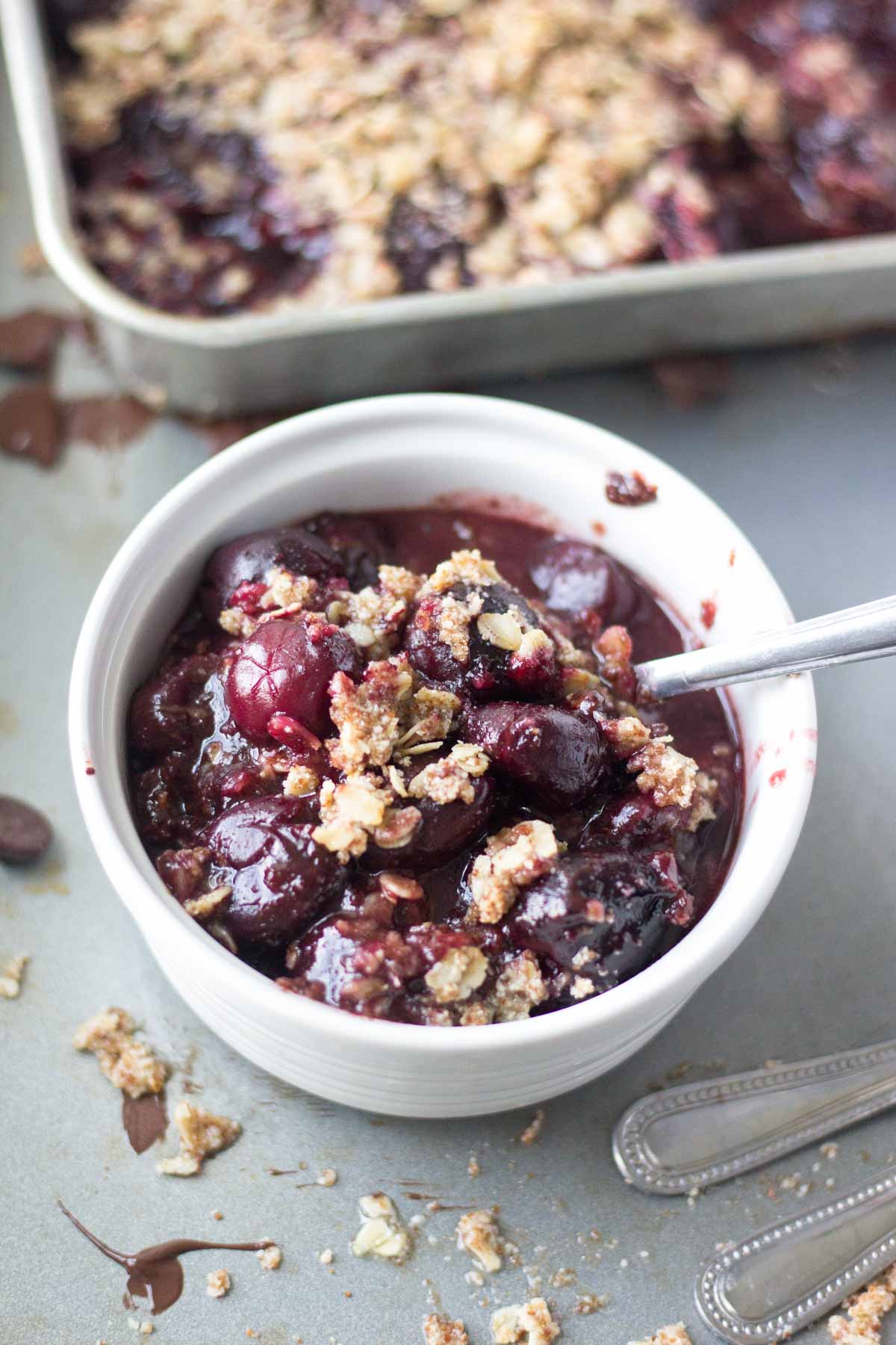 spoon resting in a ramuken filled with easy cherry crisp recipe made with frozen cherries and dark chocolate and topped with a gluten free oat crust.