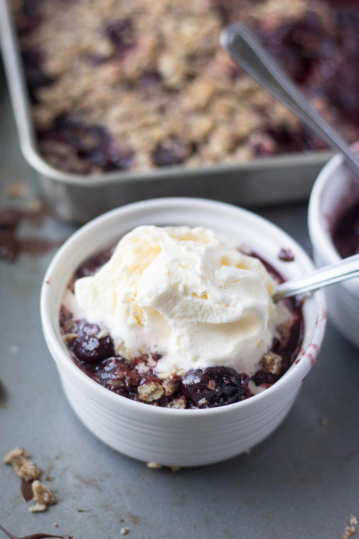 Easy cherry crisp made with frozen cherries and dark chocolate in a white ramuken with a dollop of whipped cream on top