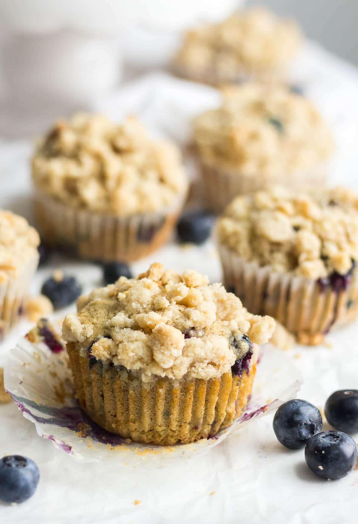 blueberry muffins with streusel crumb topping on a piece of parchment paper with the liner peeled off