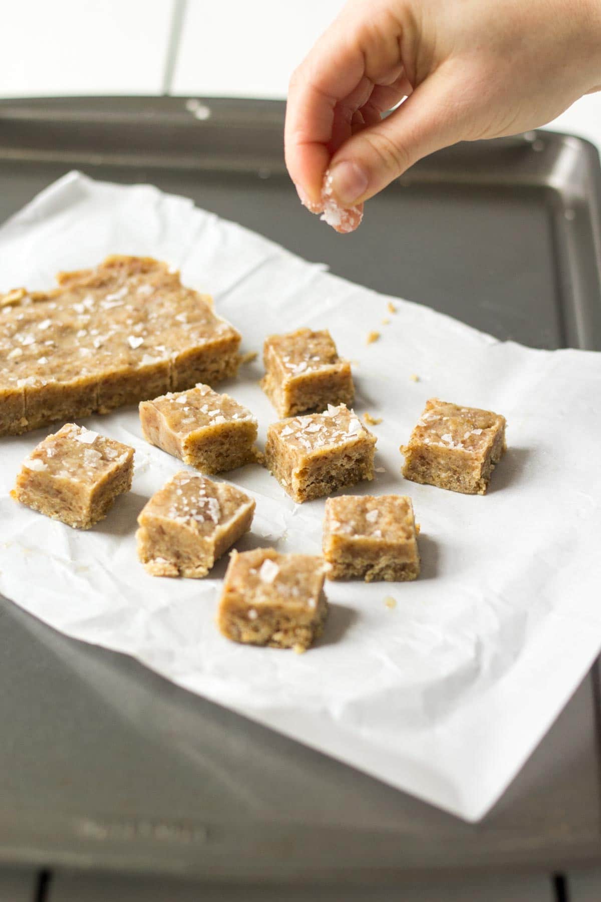 hand sprinkling sea salt over healthy salted caramels on a piece of parchment paper on a cookie sheet