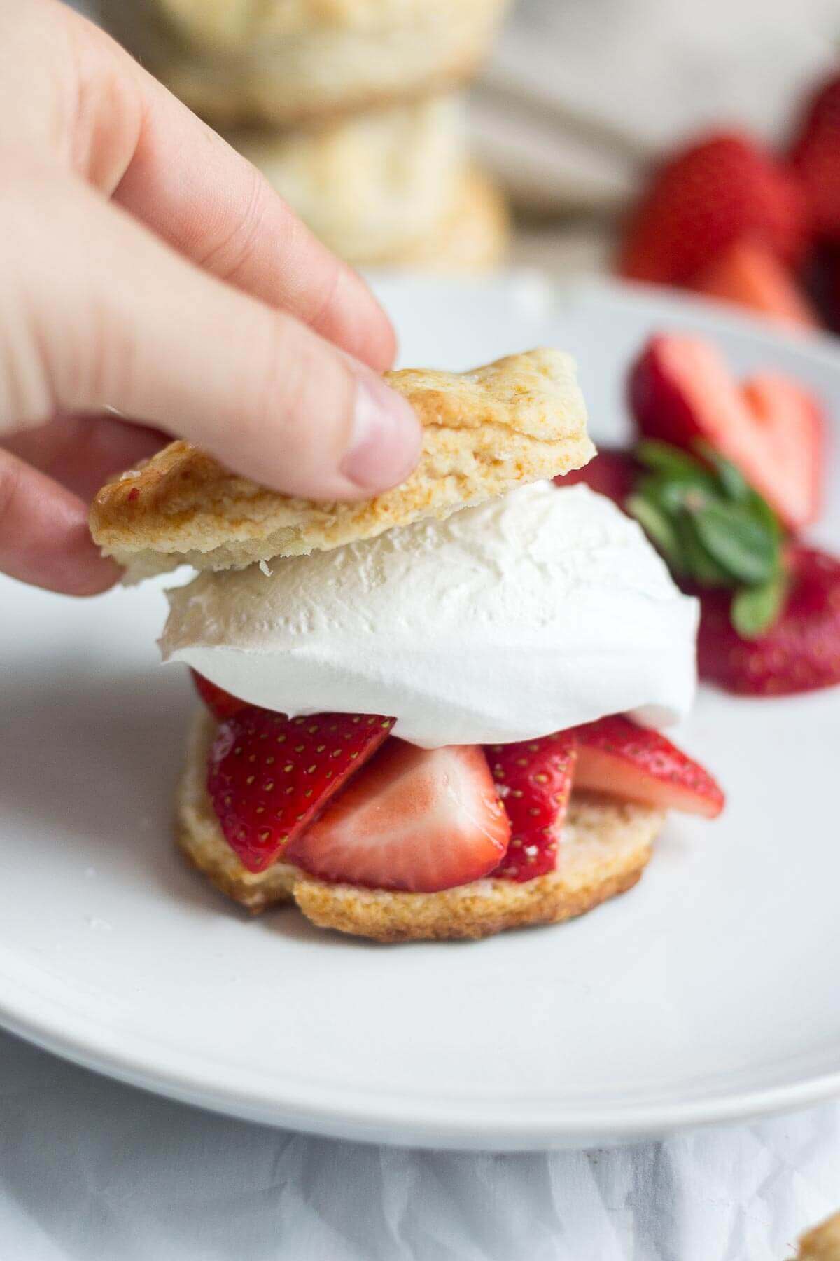 a hand placing the top portion on the Healthy strawberry shortcake