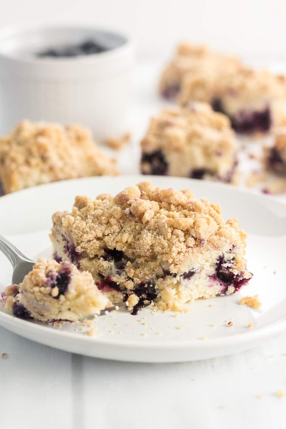 Brown Butter Blueberry Coffee Cake resting on a white plate with a fork cutting into it