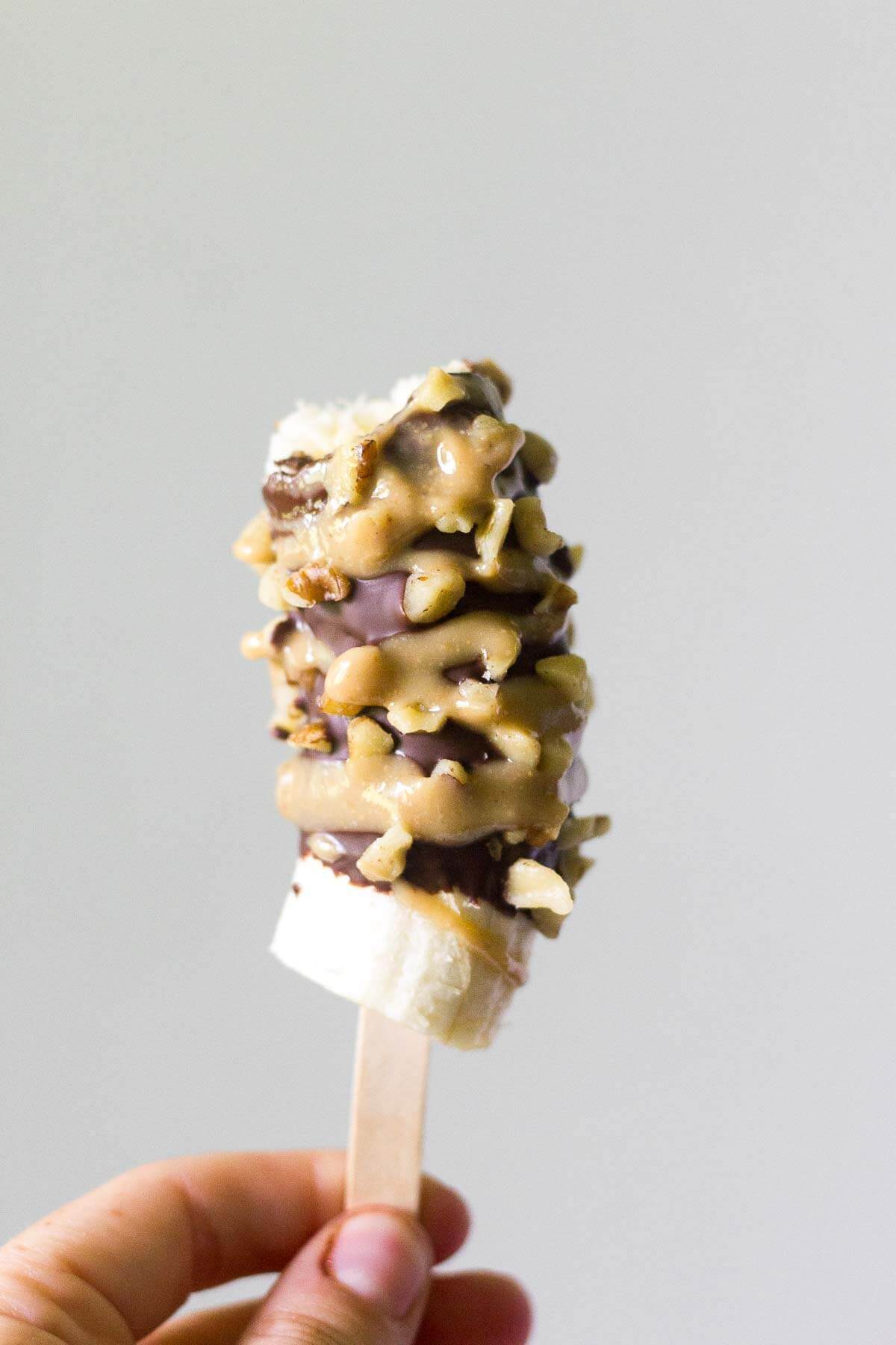 Hand holding a paleo frozen banana on a popsicle stick