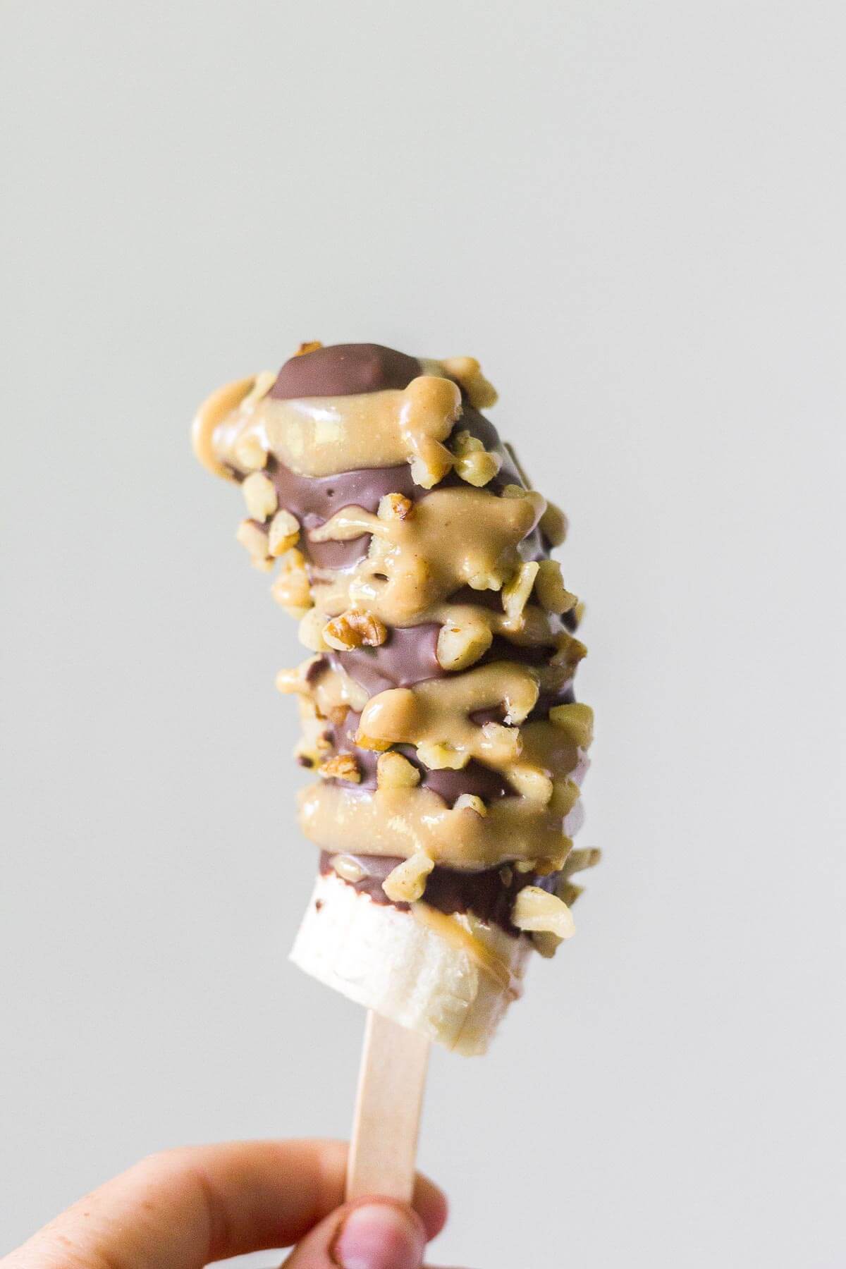 hand holding a chocolate and nut covered paleo frozen banana