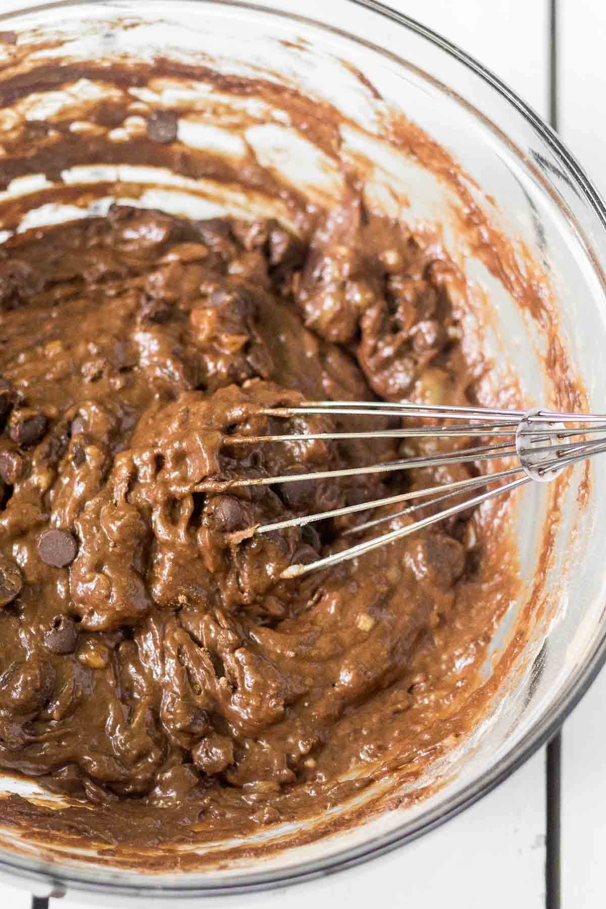 healthy chocolate chip banana bread batter in a glass mixing bowl with a whisk